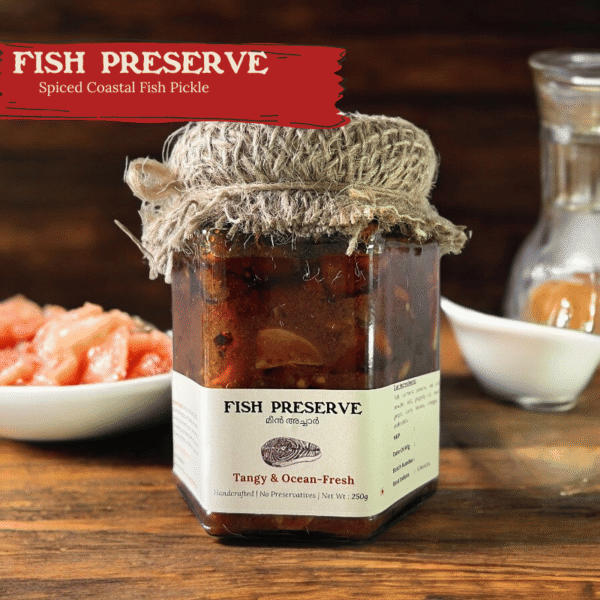 Glass jar of Spiso Fish Preserve Kerala Fish Pickle on a wooden surface with dried chilies