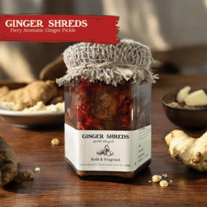 Glass jar of Spiso Ginger Shreds Pickled Ginger on a wooden surface with ginger and curry leaves